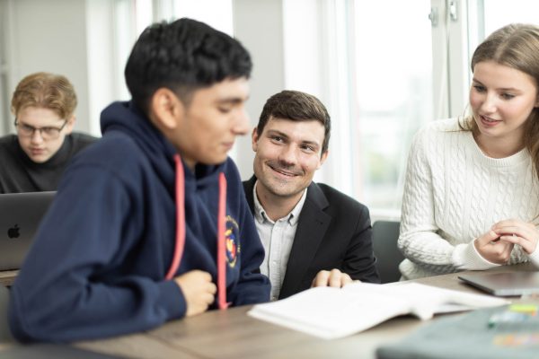 Lärare sitter på huk mellan två elever i ett klassrum