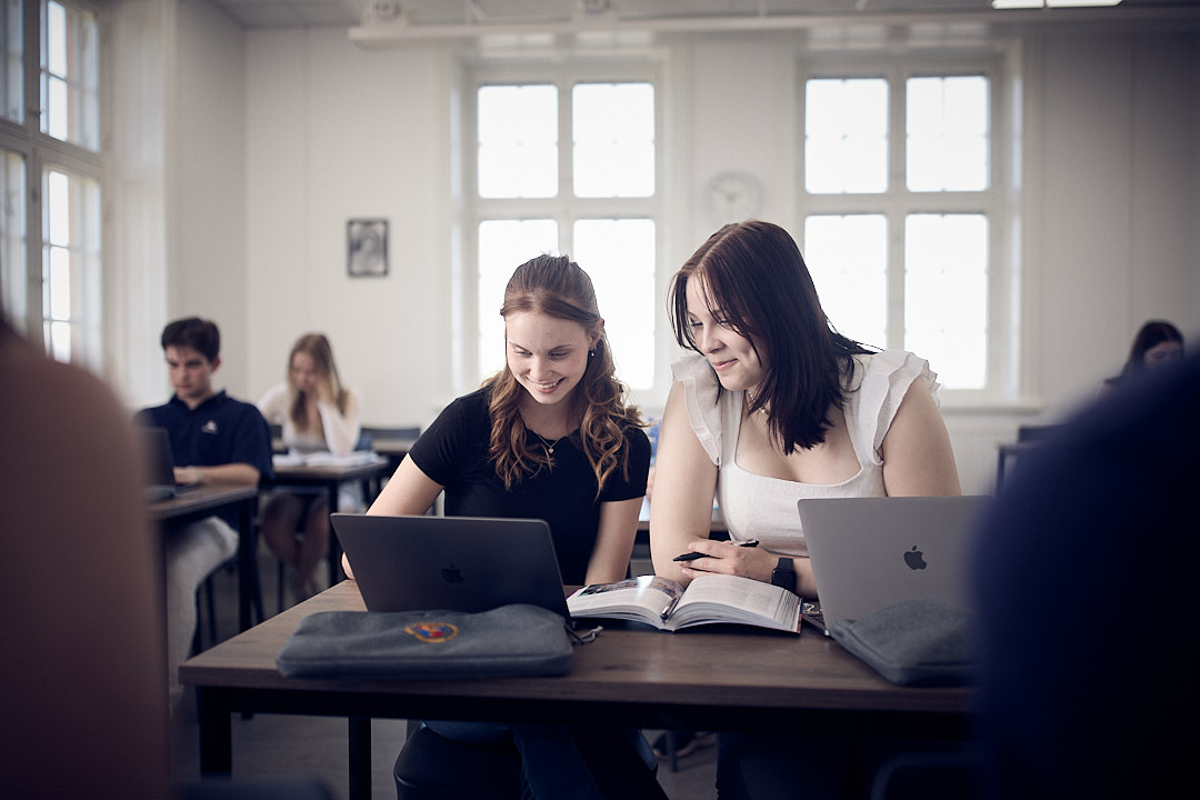Två elever samarbetar och studerar tillsammans med sina datorer i klassrummet.